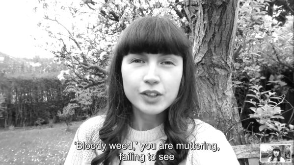 Greyscale. Poet Kirsten MacQuarrie, a white woman with long brown hair (and a severe fringe), stands outside. She says, "'Bloody weed,' you are muttering, failing to see", squinting slightly into the camera. Behind her a tree is in full bloom.